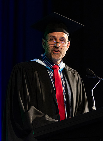 A man wearing academic regalia is standing at a podium. 